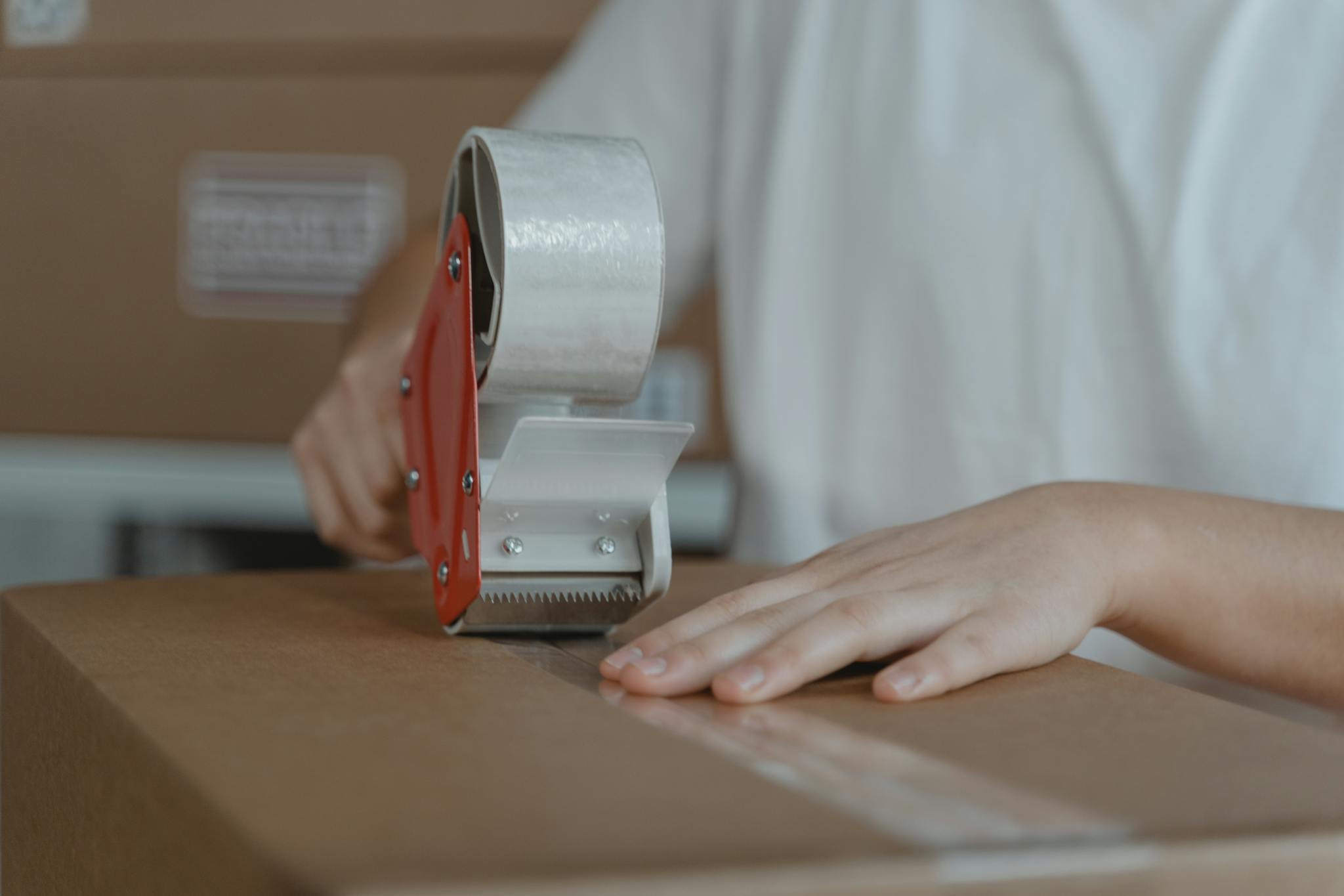 A person sealing a cardboard box with tape, emphasizing packaging and shipping processes.